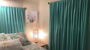 Ein Schlafzimmer mit einem Bett, einem Nachttisch mit Lampe und blaustichigen Vorhängen.
