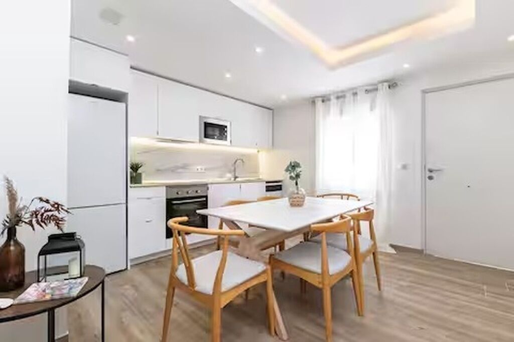 A modern kitchen with white cabinets, a dining table with chairs, and a small island with a microwave.