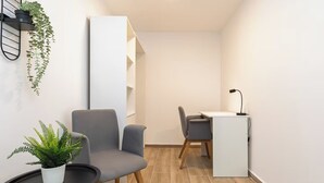 Et moderne værelse med en grå lænestol, et rundt bord med en potteplante, et hvidt skrivebord med stol og en sort lampe.