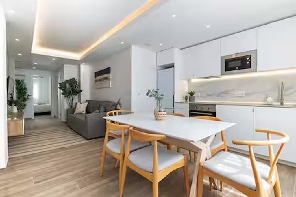 A modern kitchen with white cabinets, a microwave, and a dining area with a table and chairs.