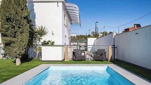 En swimmingpool med en hvid væg og en lille terrasse med to stole og et bord.