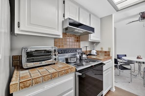 A modern kitchen with white cabinets, a built-in toaster, a stove, and a tiled backsplash. - NEW! Charming Downtown Palm Springs Getaway (Palm Springs)