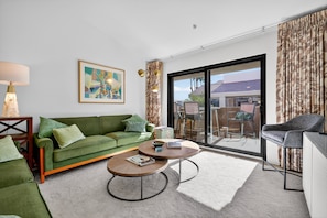 A modern living room with a green sofa, two round coffee tables, a lamp, and a large window with curtains. - NEW! Charming Downtown Palm Springs Getaway (Palm Springs)