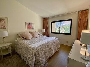 A bedroom with a bed, a nightstand, a desk, a window, and a painting on the wall. - NEW! Charming Downtown Palm Springs Getaway (Palm Springs)