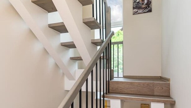 Eine moderne Treppe mit Holzdielen und schwarzen Geländern, die zu einem Raum mit einem großen Fenster und einem gerahmten Bild an der Wand führt.