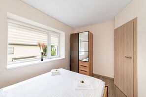 Ein Schlafzimmer mit einem Bett, einem Fenster mit Jalousien, einem Kleiderschrank und einem Spiegel.