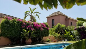 En swimmingpool med flisekant, omgivet af frodig vegetation og blomstrende planter.