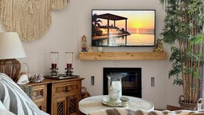En hyggelig stue med et fjernsyn, der viser et solnedgangsmotiv, en pejs, et træskab og en behagelig sofa.