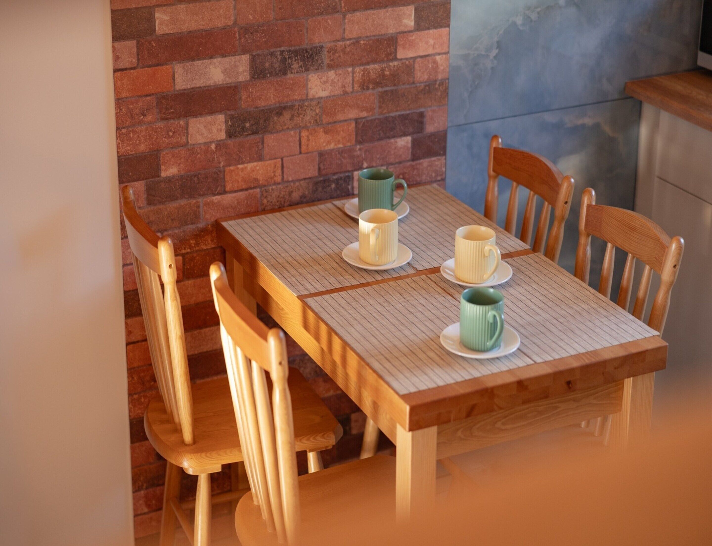 Una mesa de madera para comer con cuatro sillas, una pared de ladrillo y un salpicadero de azulejos.