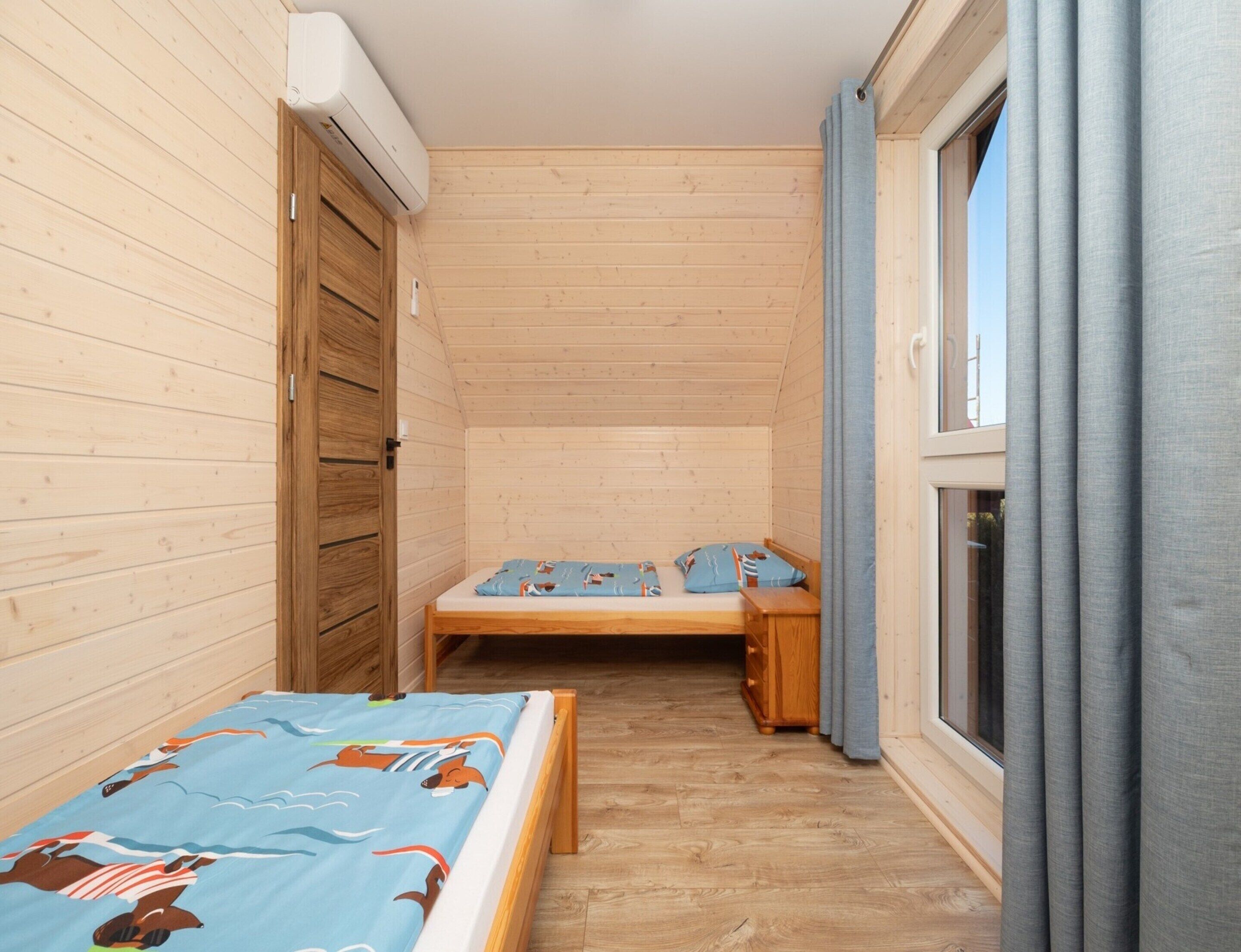 Ein kleiner, schmaler Raum mit Holzwänden und einem Einzelbett mit blau gemustertem Bettbezug.