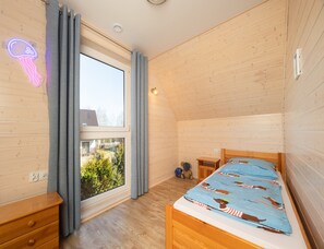 A bedroom with a wooden ceiling, a bed with a blue patterned bedspread, a nightstand, a dresser, and a window with curtains. - Year-round Holiday Home With Fireplace and Terrace (Mielno)