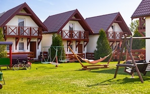 A row of chalet-style buildings with balconies, a swing set, and a hammock in a grassy yard. - Year-round Holiday Home With Fireplace and Terrace (Mielno)