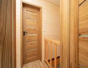 A wooden door with horizontal slats and a metal handle, leading to a room with wooden walls and a wooden railing. - Year-round Holiday Home With Fireplace and Terrace (Mielno)