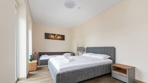 A modern hotel room with two beds, a wooden floor, a painting on the wall, and a bedside table with a lamp.