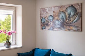 Une pièce avec une fenêtre, un vase rempli de fleurs roses et un canapé bleu.