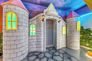 Ein spielbereich im Burgstil mit Steinmauern, Bogenfenstern und einer zentralen Tür.