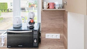 Una cucina con macchina da caffè, forno a microonde e pensile con bicchieri da vino e tazze.