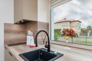 A modern kitchen with a black sink, a window with a view of a house, and a vase with flowers.