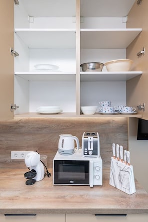 A kitchen with a microwave, toaster, kettle, and knife block on a wooden countertop.