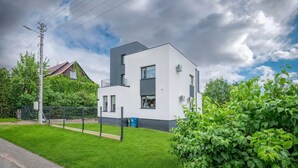A modern two-story house with a flat roof, a balcony, and a fenced yard.