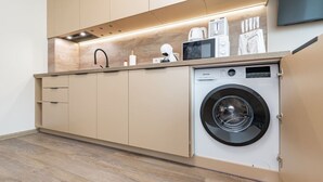 A compact kitchen with a built-in washing machine, wooden cabinets, and a countertop with various appliances.