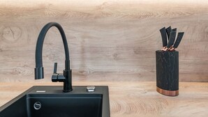 A modern kitchen with a black sink, a curved faucet, and a marble vase with utensils.