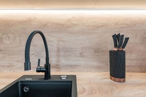 A modern kitchen with a black sink, a curved faucet, and a marble vase with utensils.