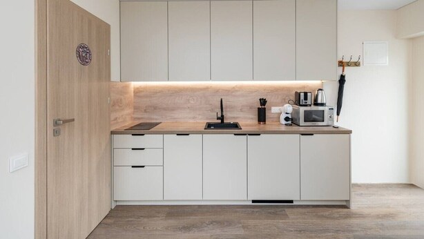 A modern kitchen with a wooden door, white cabinets, a built-in microwave, and a coffee maker.