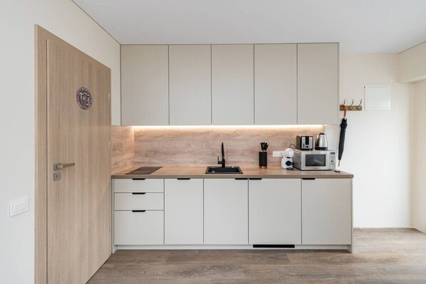 Une cuisine moderne avec une porte en bois, des placards blancs, un four à micro-ondes encastré et une machine à café.