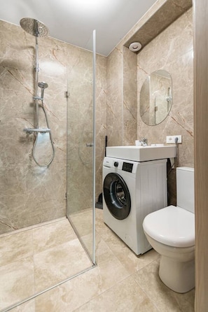 Un baño con ducha envuelta en vidrio, lavadora y retrete.
