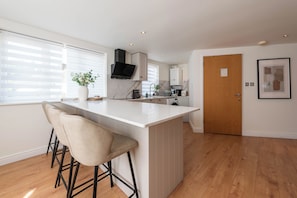 Een moderne keuken met een centraal eiland, barkrukken, een groot raam en een deur.