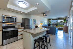 A modern kitchen with a central island, built-in appliances, and a dining area with a view. - Maui Banyan H406 | 1BR/2BA Kihei Condo with Lanai, Pool, AC & South Maui Locatio (Kihei)