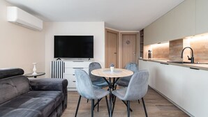 A modern living room with a sofa, a round dining table with chairs, a flat-screen TV, and a kitchen area with a countertop and sink.