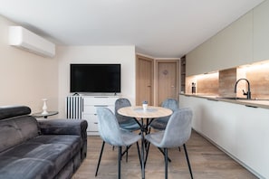 Una sala moderna con un sofá, una mesa de comedor redonda con sillas, un televisor de pantalla plana y una cocina con encimera y lavamanos.