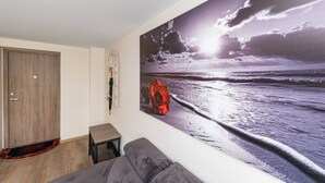 A room with a large beach painting, a grey sofa, a wooden door, and a small stool.