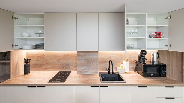 A modern kitchen with a built-in stove, sink, and coffee machine, featuring light wood cabinetry and open shelving.