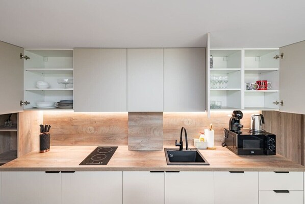 Eine moderne Küche mit Einbauherd, Spüle und Kaffeemaschine, ausgestattet mit hellen Holzschränken und offenen Regalen.