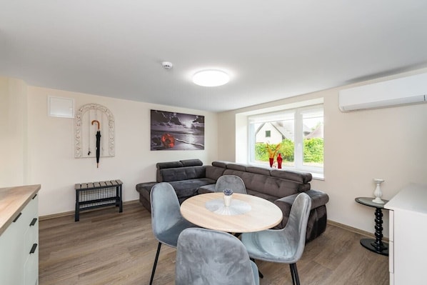 A modern living room with a grey sofa, a round wooden table, and a dining area with grey chairs.