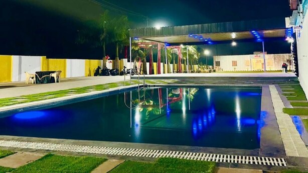 A swimming pool with a surrounding deck, a covered seating area, and a building in the background.