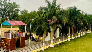 A covered outdoor seating area with a red roof, surrounded by palm trees and a well-maintained lawn. - Kanha Green (Bhopal)