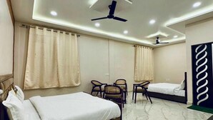 A modern hotel room with a bed, two chairs, a desk, a ceiling fan, and a decorative wall panel. - Kanha Green (Bhopal)
