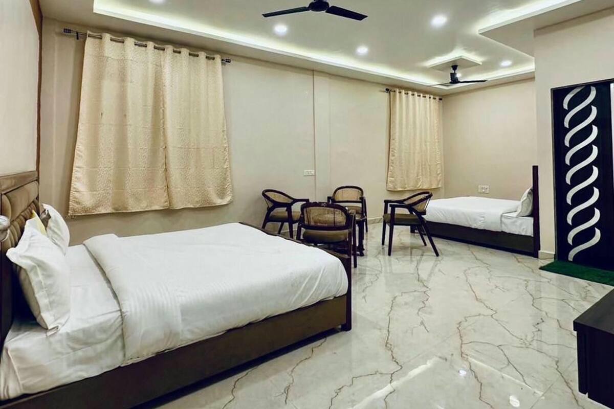 Una habitación de hotel moderna con cama, dos sillones, escritorio, ventilador de techo y un panel decorativo en la pared.
