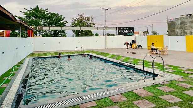 A swimming pool with a tiled deck, surrounded by a white wall and a green lawn. - Kanha Green (Bhopal)