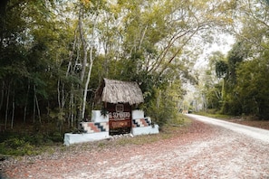 Una estructura rústica con techo de paja identificada como 'El Sombrero Ecological Lodge', con un sendero de tierra que atraviesa un bosque.
