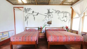 Una habitación con dos camas de madera, un mural en la pared y una ventana con cortinas.