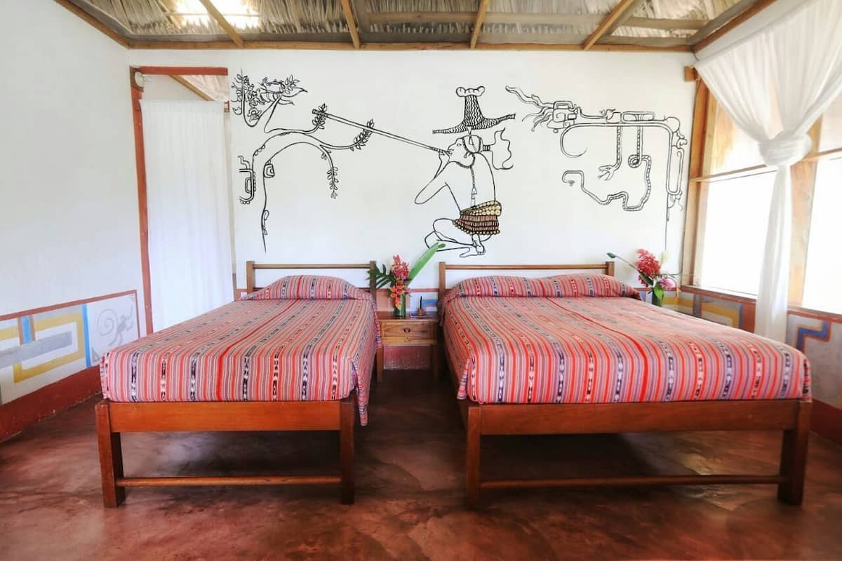 A room with two wooden beds, a mural on the wall, and a window with curtains.