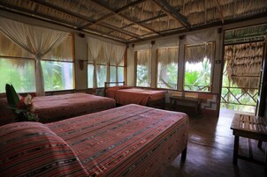 Quarto com quatro camas, janelas amplas e telhado de palha.