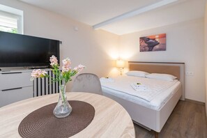 Ett hotellrum med en säng, en tv, en vas med blommor och en tavla på väggen.