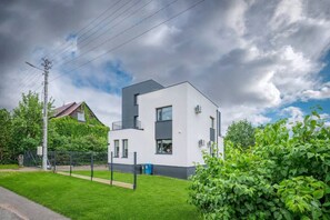 Ein modernes, zweistöckiges Haus mit flachem Dach, einem sichtbaren Balkon und einem gepflegten Rasen.