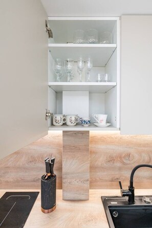 Eine moderne Küche mit einer eingebauten Schrankwand, die Gläser und Keramiktassen präsentiert, einem zentralen schwarzen Marmorblock und einem Waschbecken mit schwarzem Wasserhahn.